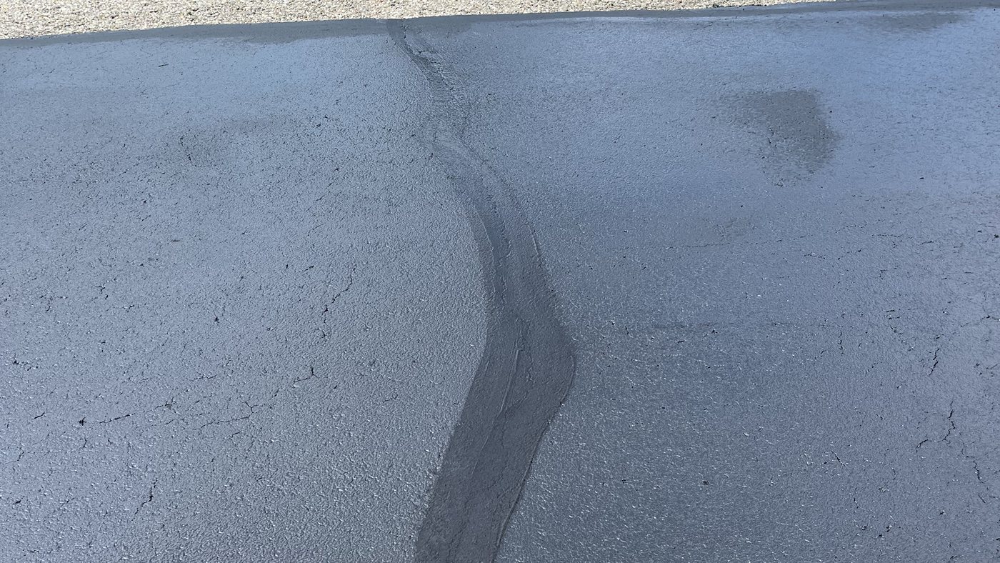 A filled crack in an asphalt driveway, sealed over with fresh sealer