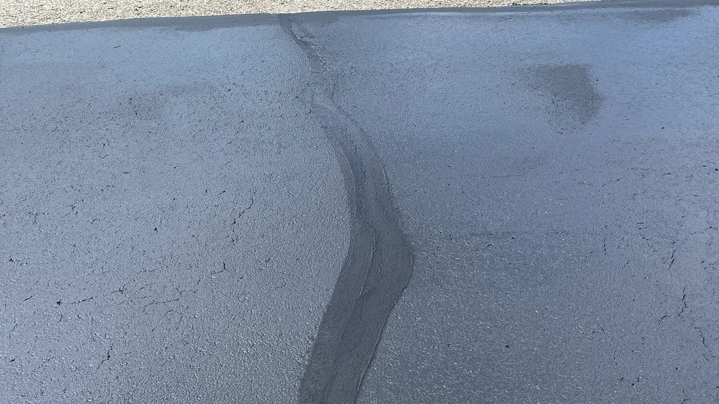 A filled crack in an asphalt driveway, sealed over with fresh sealer