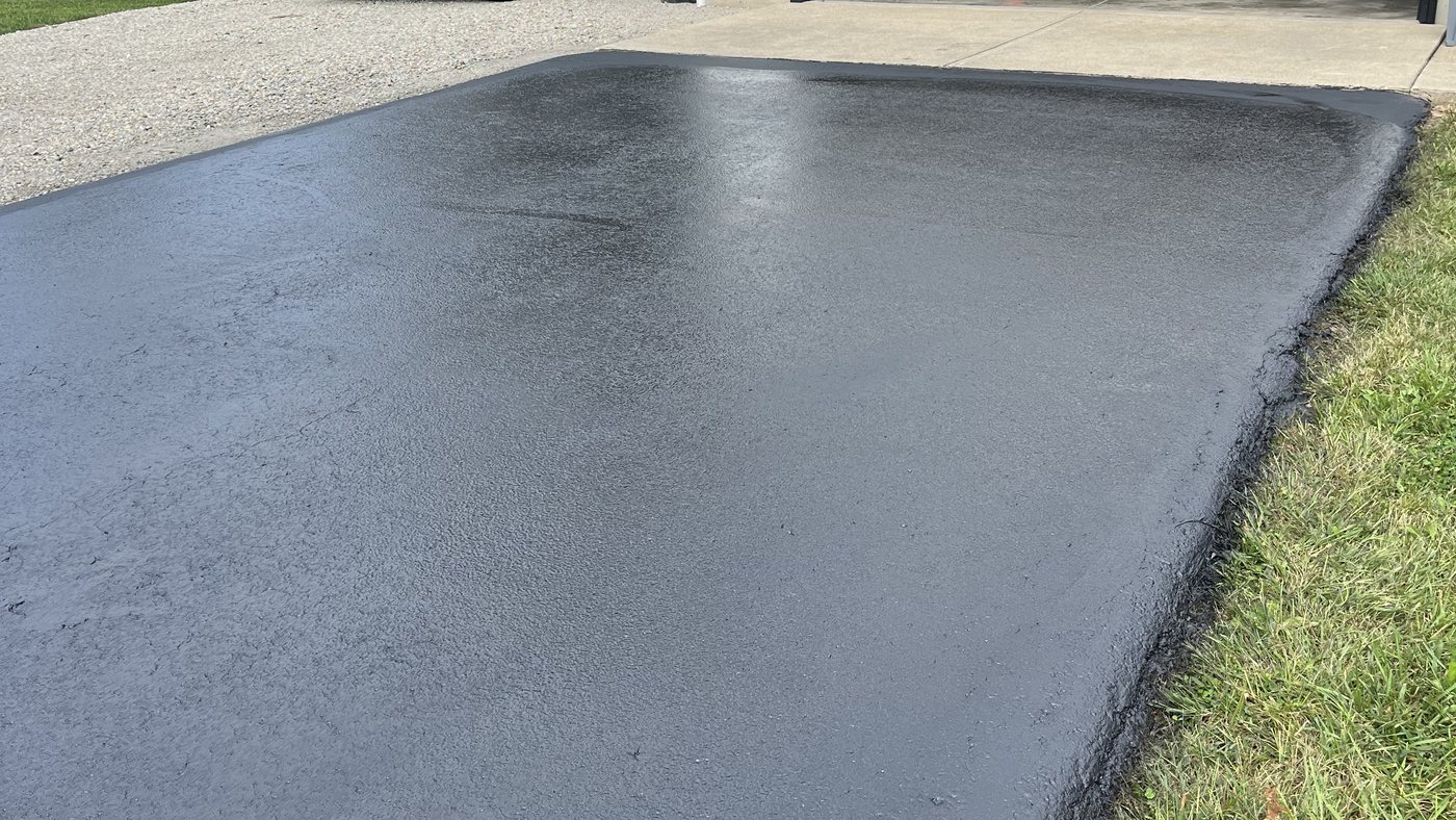 A freshly sealed asphalt driveway in front of a garage