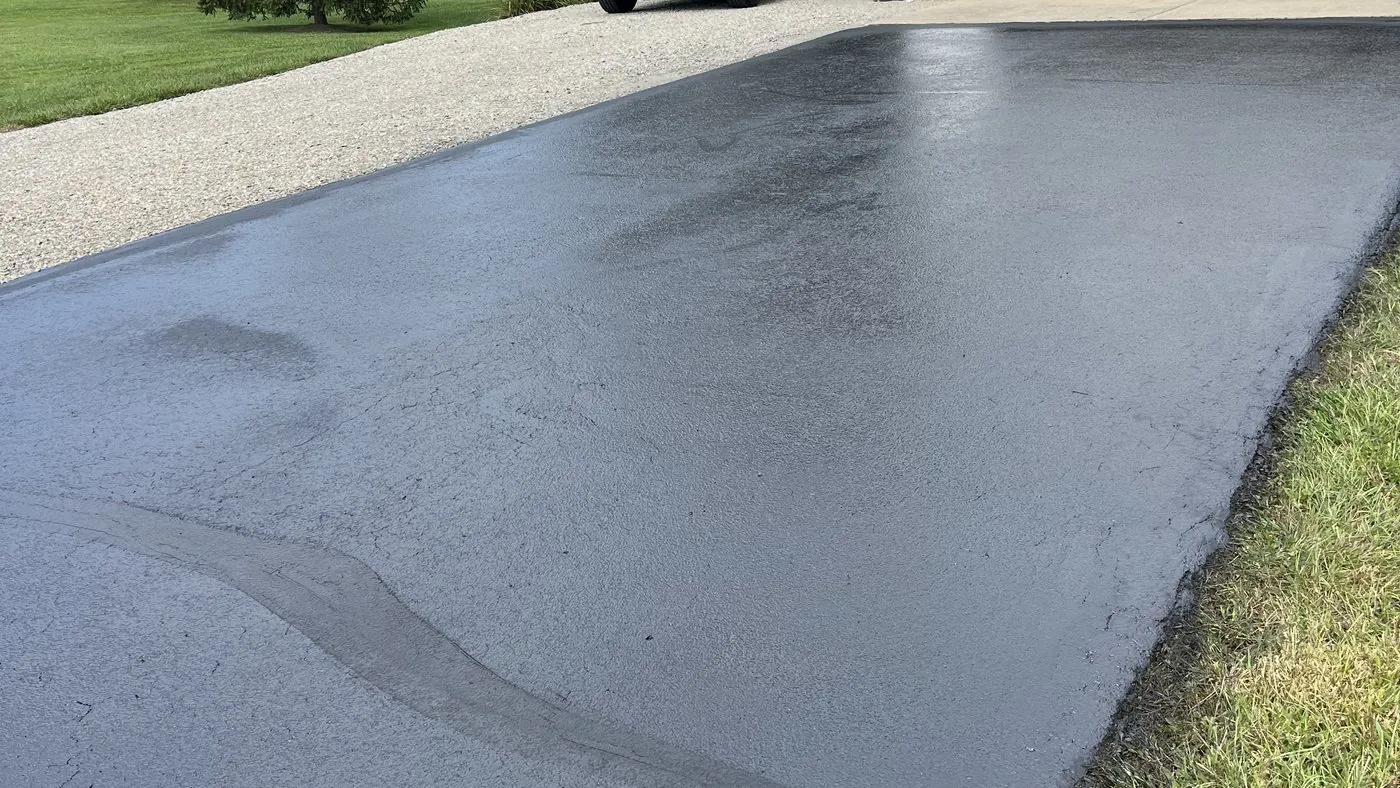 The edge of a freshly sealed driveway, cut in clean against the grass