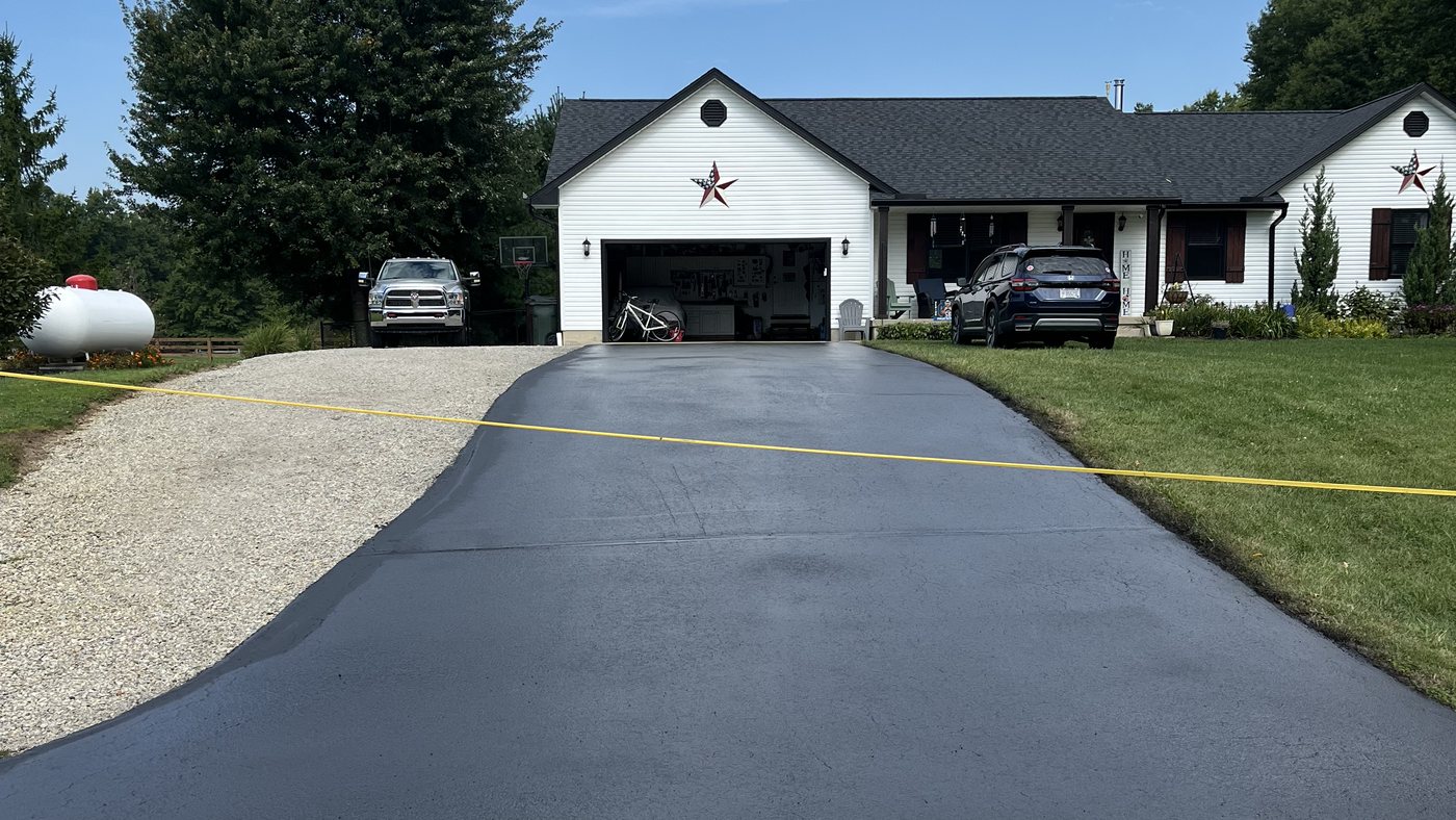A finished sealcoated driveway taped off to cure, with the house behind it